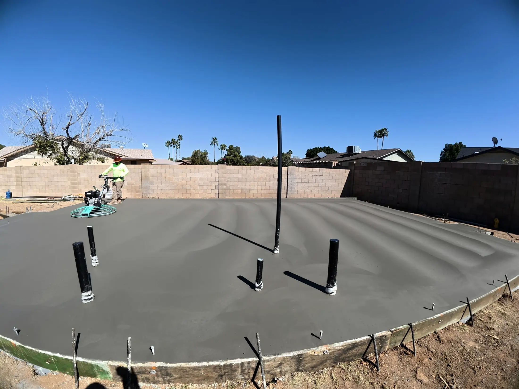A fresh slab with plumbing stubs while a power trowel runs